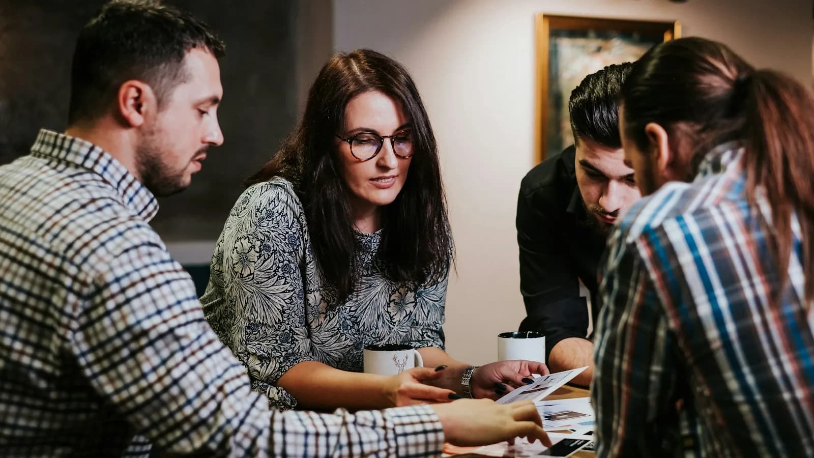 Four colleagues around a wooden table reviewing printed documents together