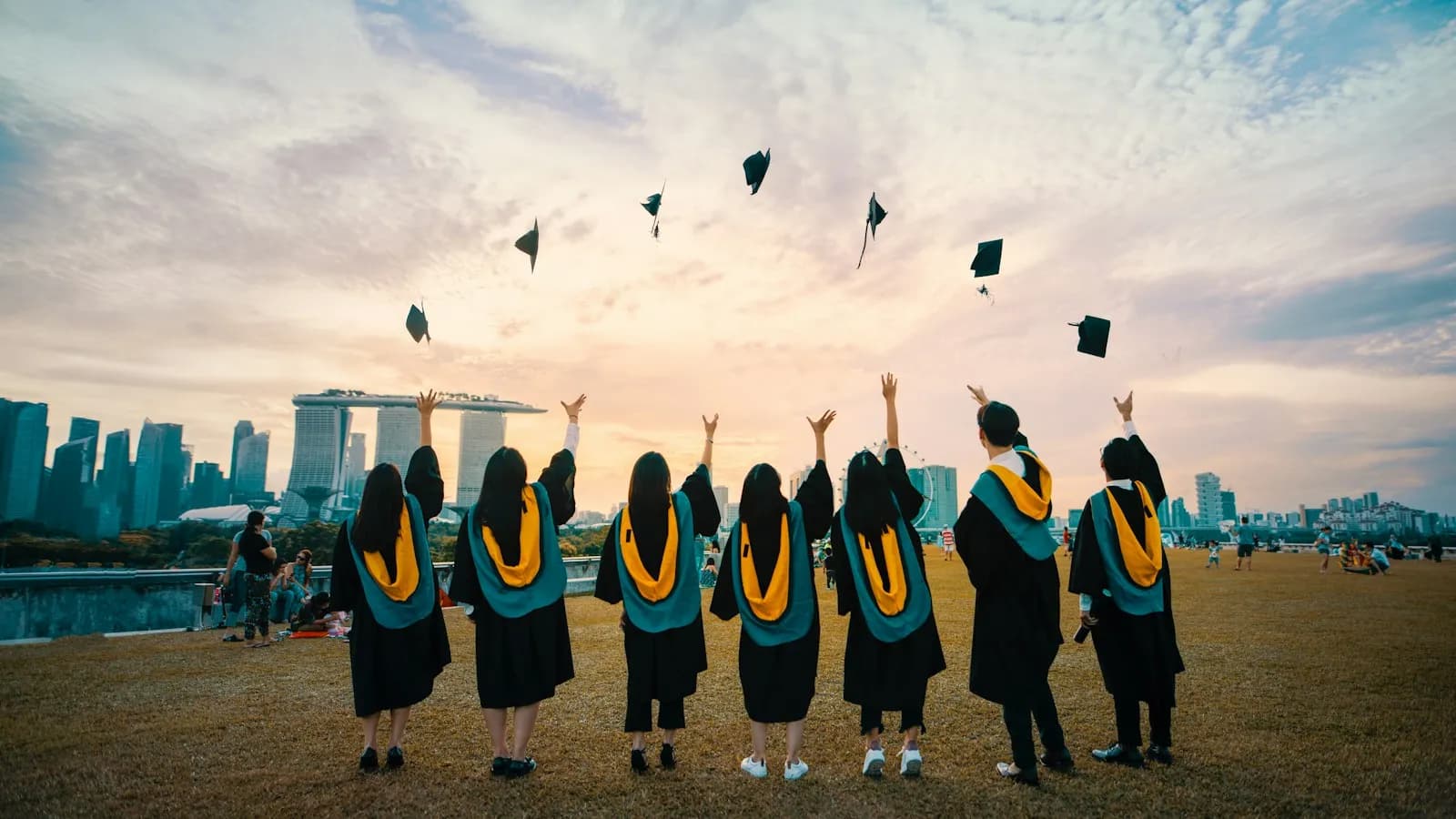 Graduates in black gowns throwing their caps into the air against a city skyline at sunset