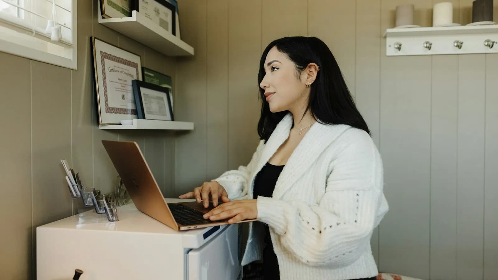 A woman working at a desk on a laptop in a home office