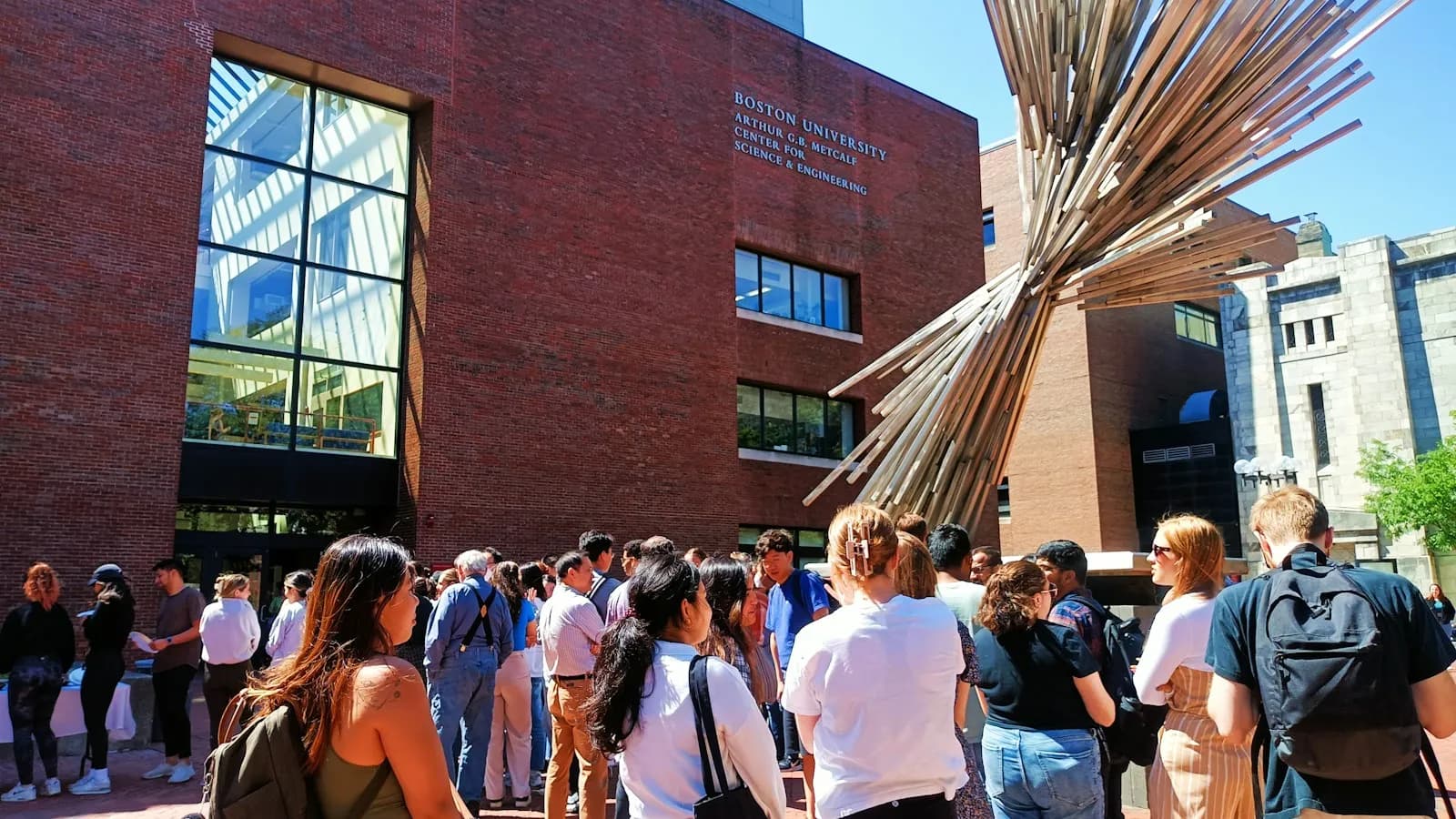 A large group of students and parents gathered outside a campus building on a sunny day