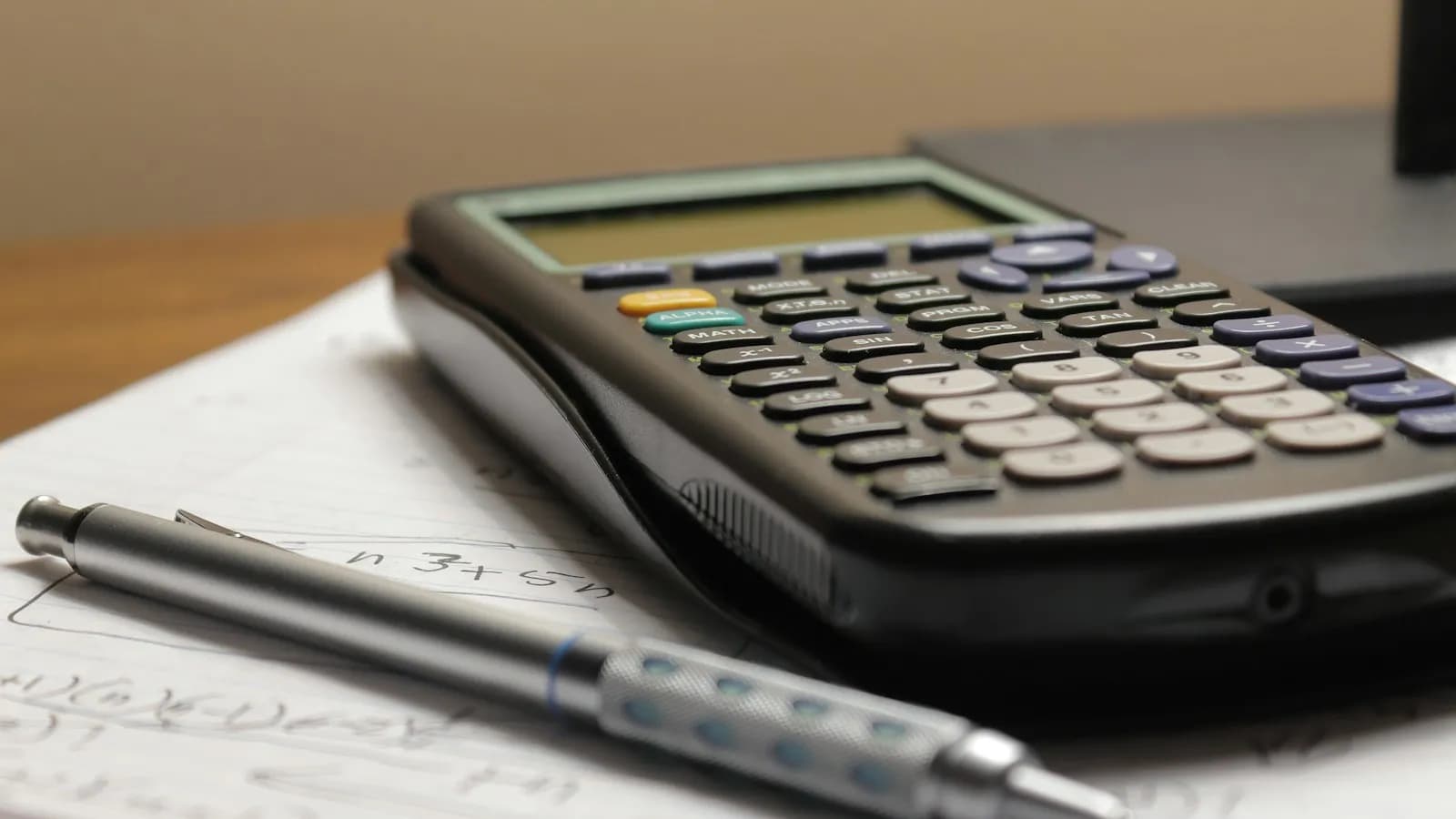 A calculator and a mechanical pencil resting on a sheet of handwritten figures