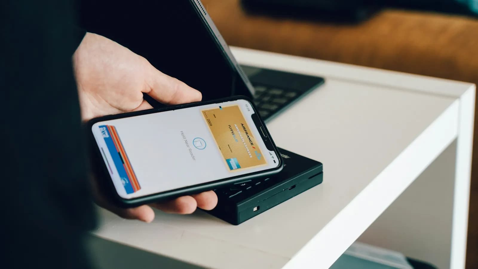 A person holding a smartphone over a card reader to make a contactless payment