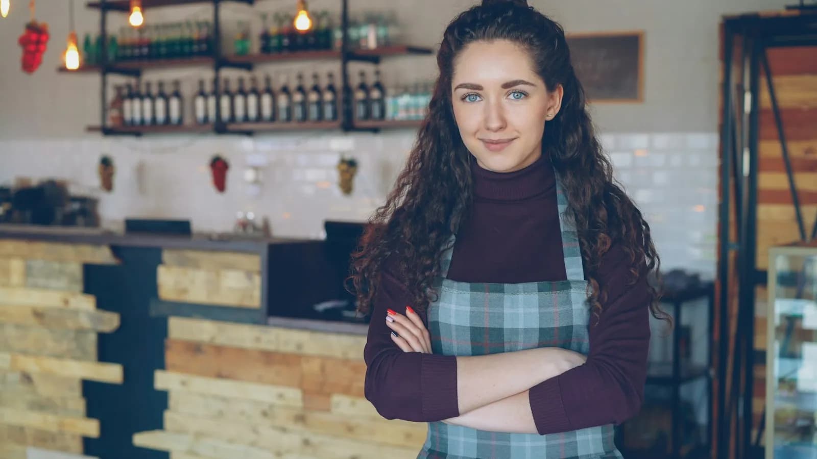 A smiling cafe owner in an apron standing in her coffee shop