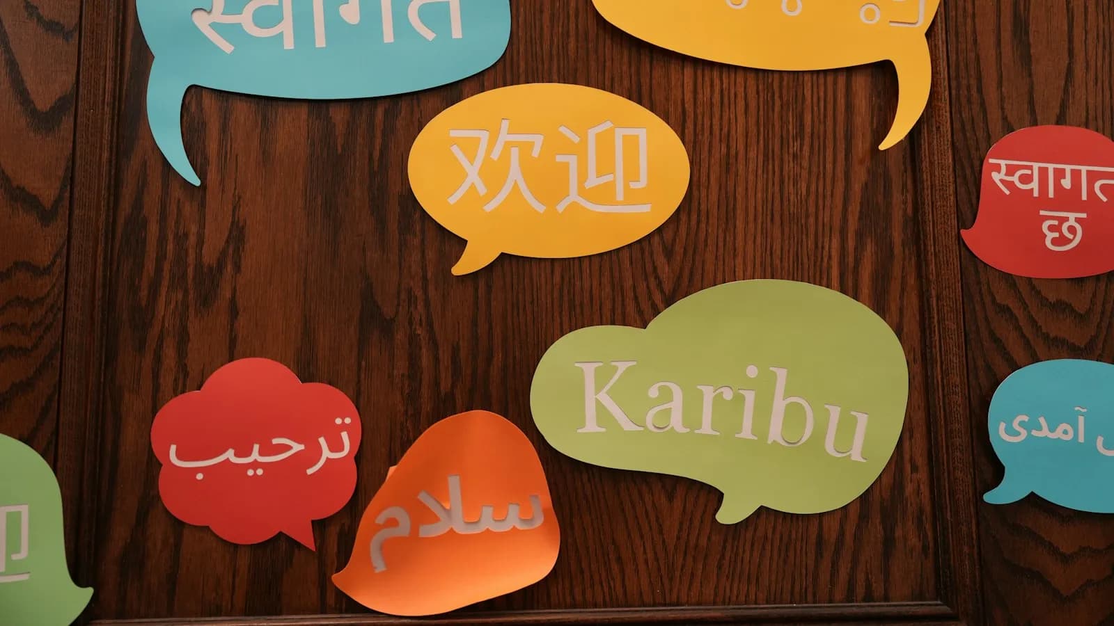 Colourful paper speech bubbles on a wooden wall with greetings in many languages