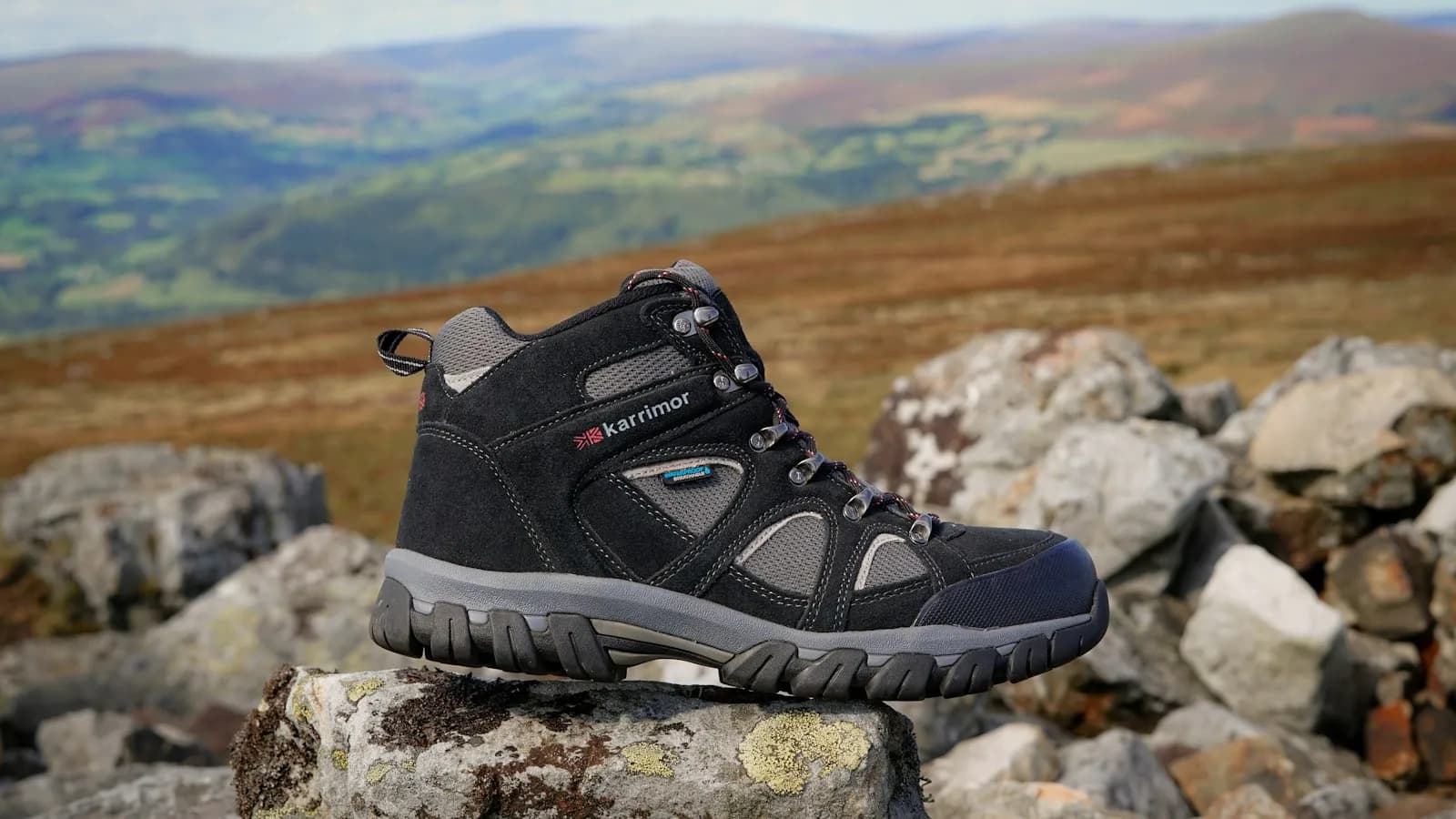 A hiking boot standing on a rock with green hills in the background