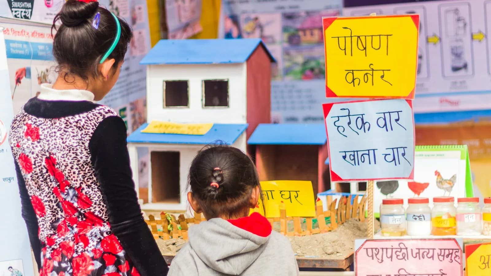 Children looking at a model house and a hand-lettered educational display at a school exhibition