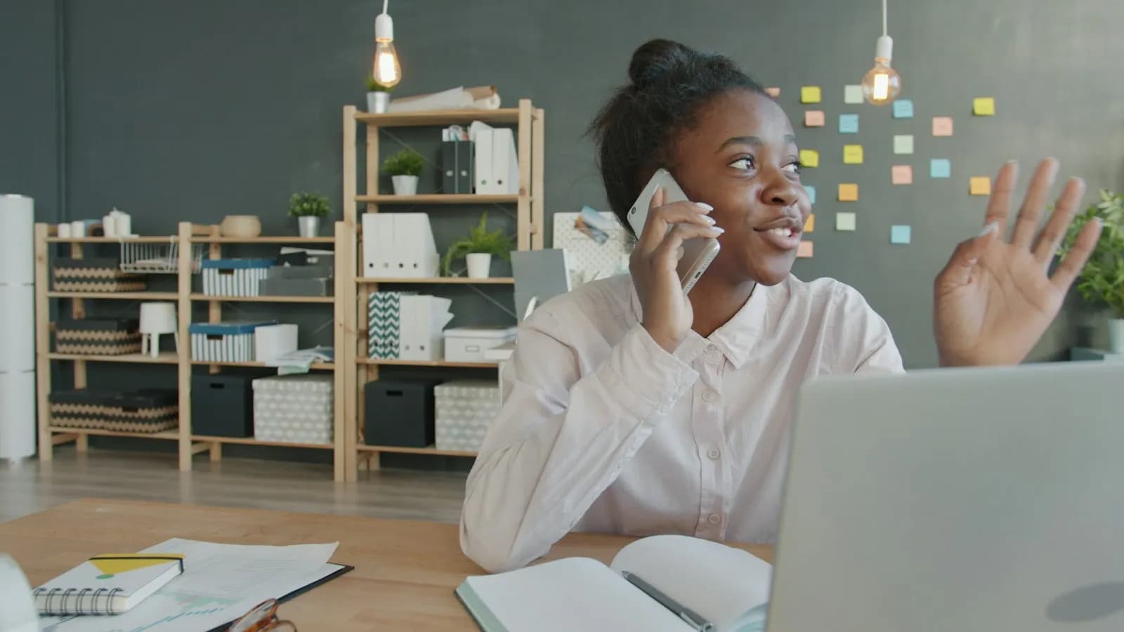 A woman talking on her phone at a desk with a laptop and sticky notes