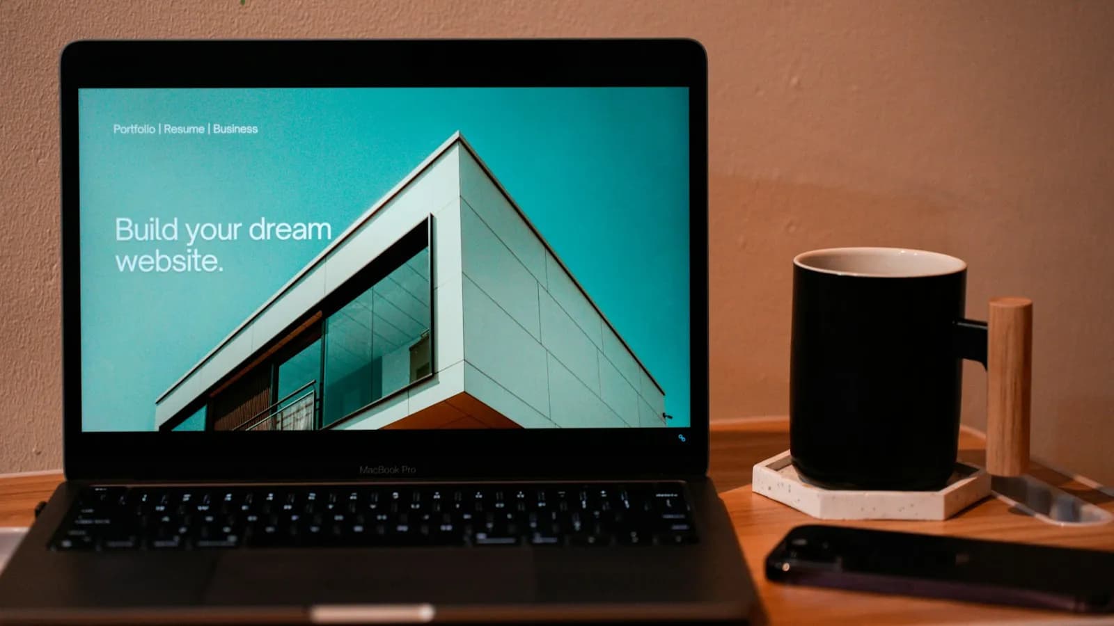 A laptop on a wooden desk showing a simple website home page next to a coffee mug