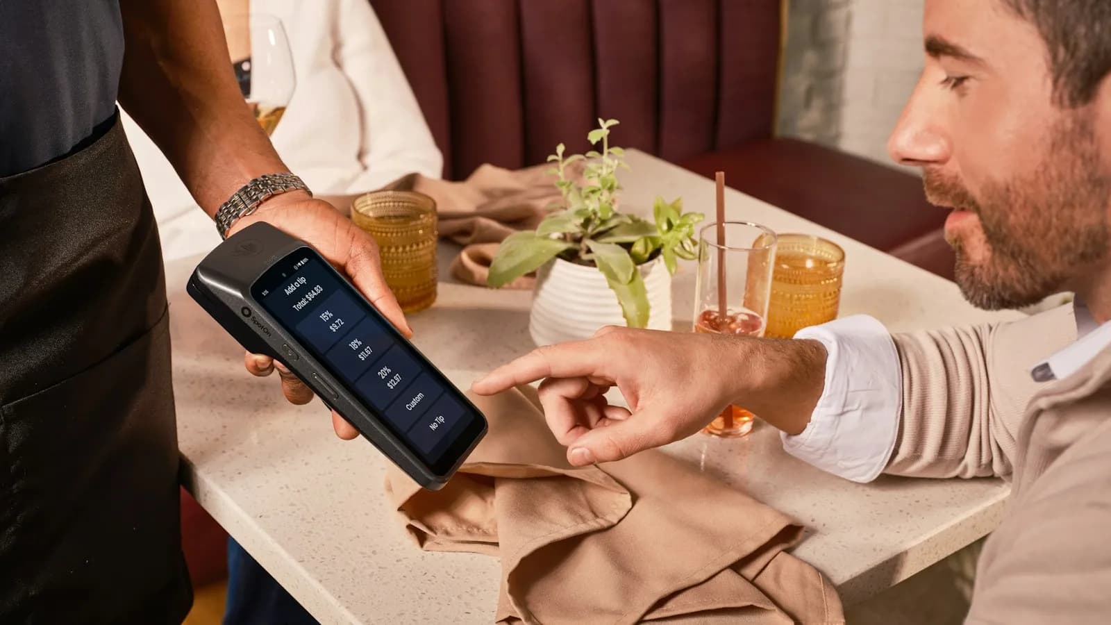 A man paying at a restaurant table while a staff member holds a handheld payment device