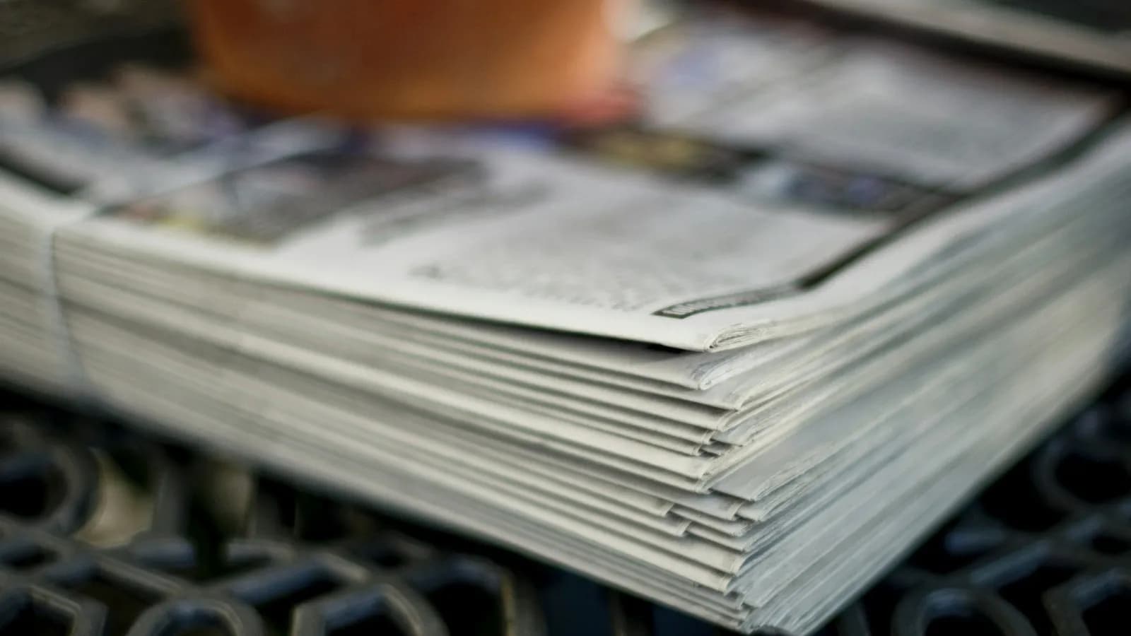 A thick stack of folded newspapers on a table, softly out of focus