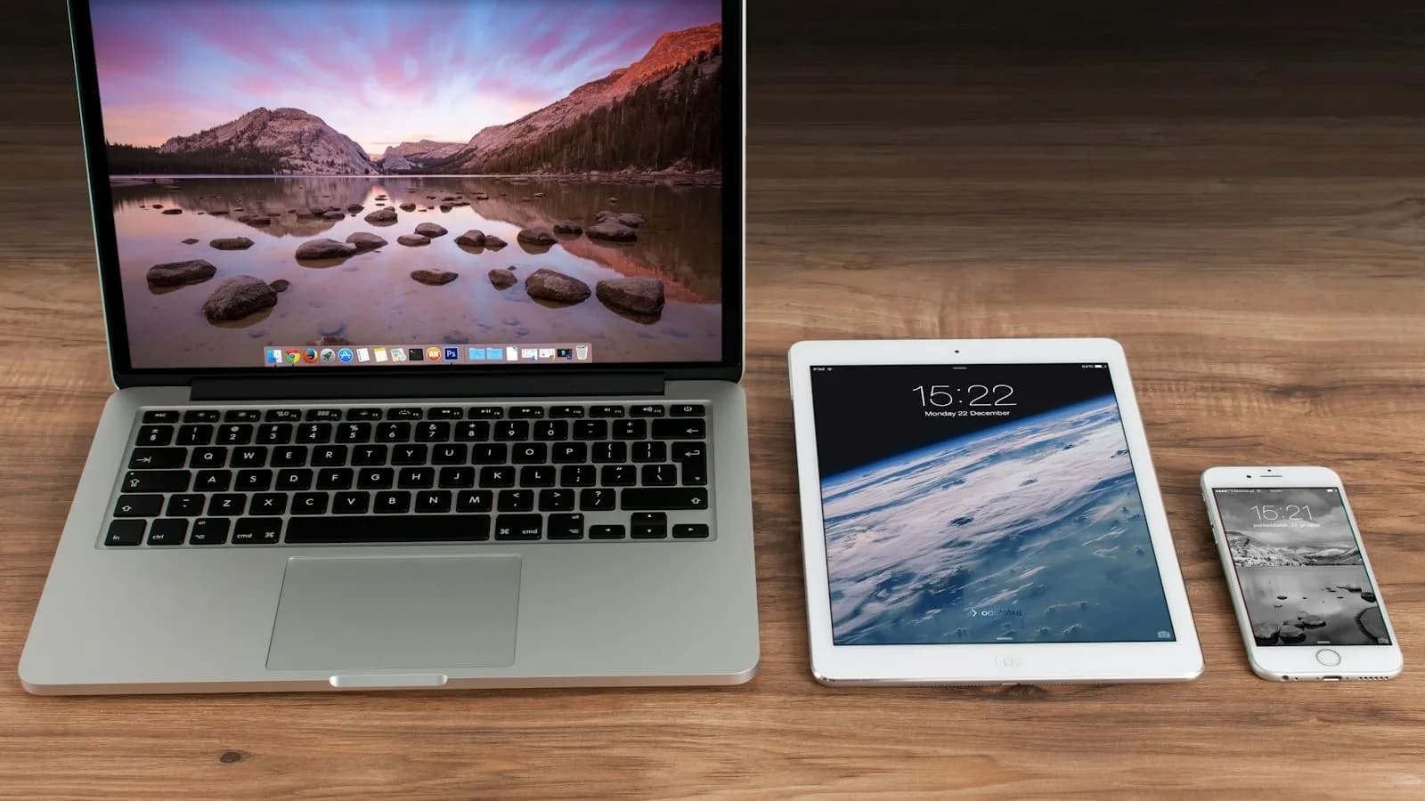 A laptop, a tablet and a phone side by side on a wooden desk