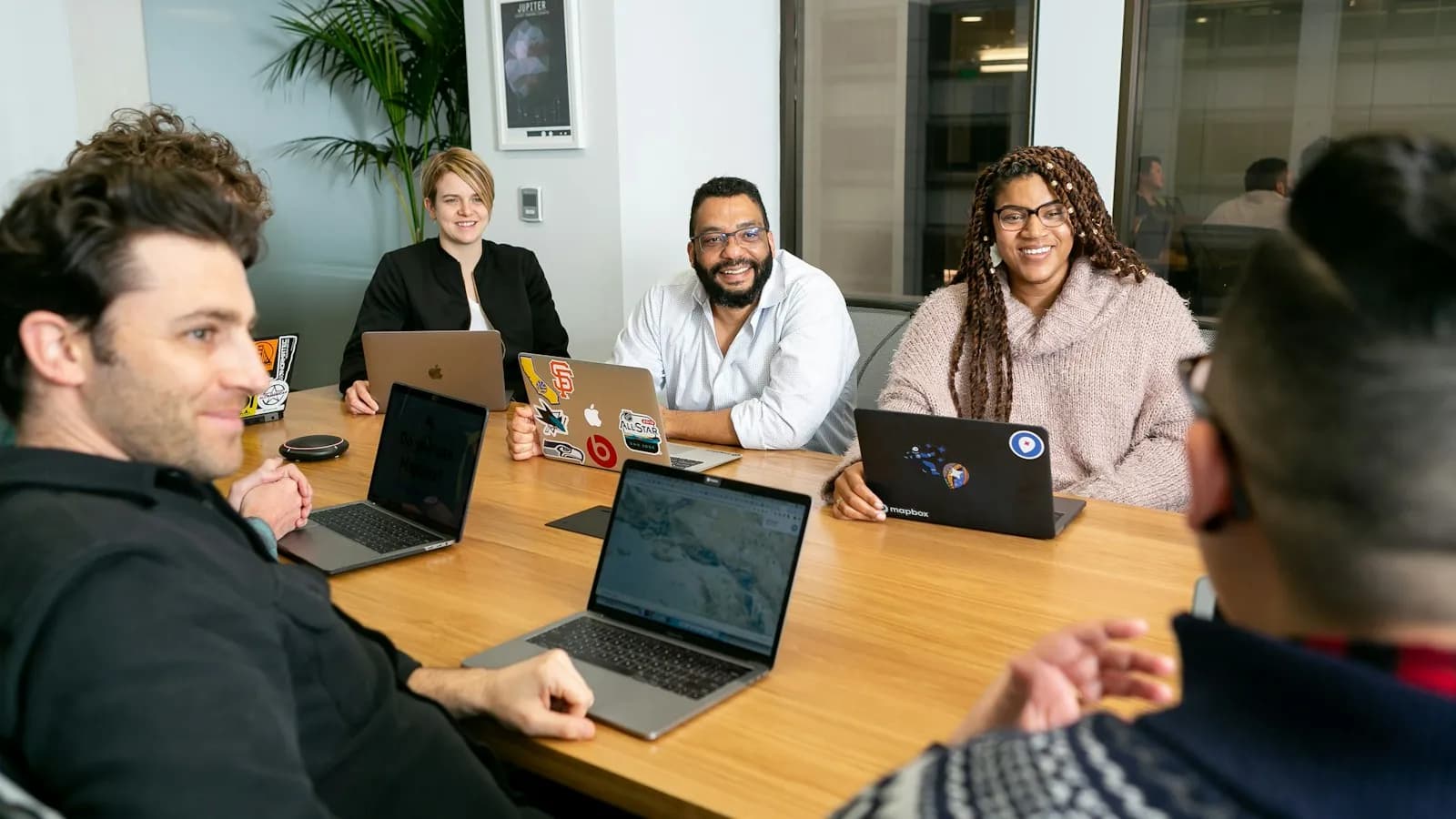 Five colleagues with laptops around a meeting table, smiling during a discussion