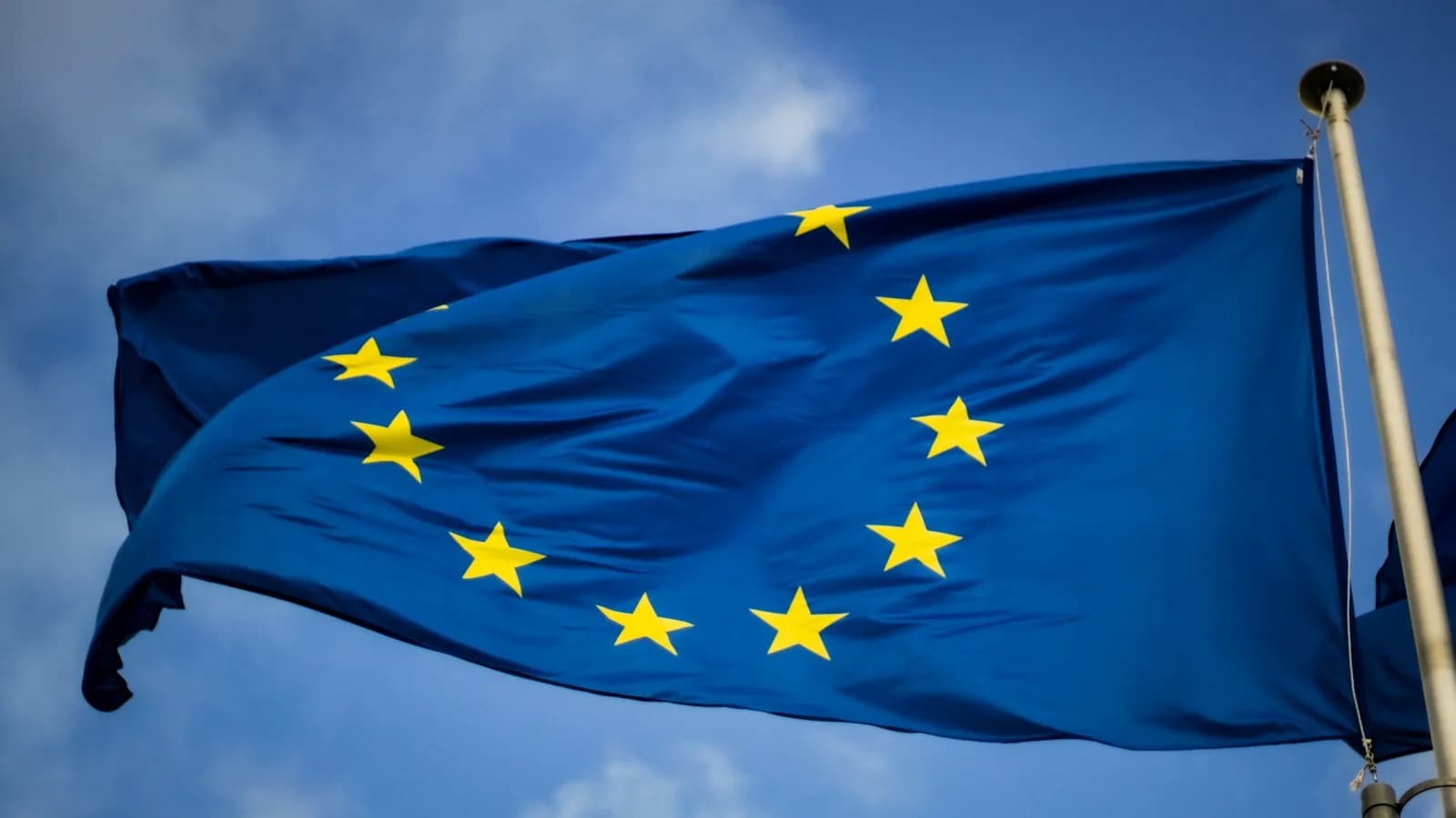The blue European Union flag with yellow stars waving against a blue sky