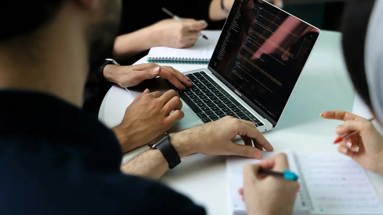 Several people working together around a laptop and notebooks