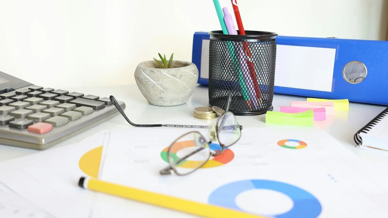 A desk with a calculator, glasses, printed charts and a blue file
