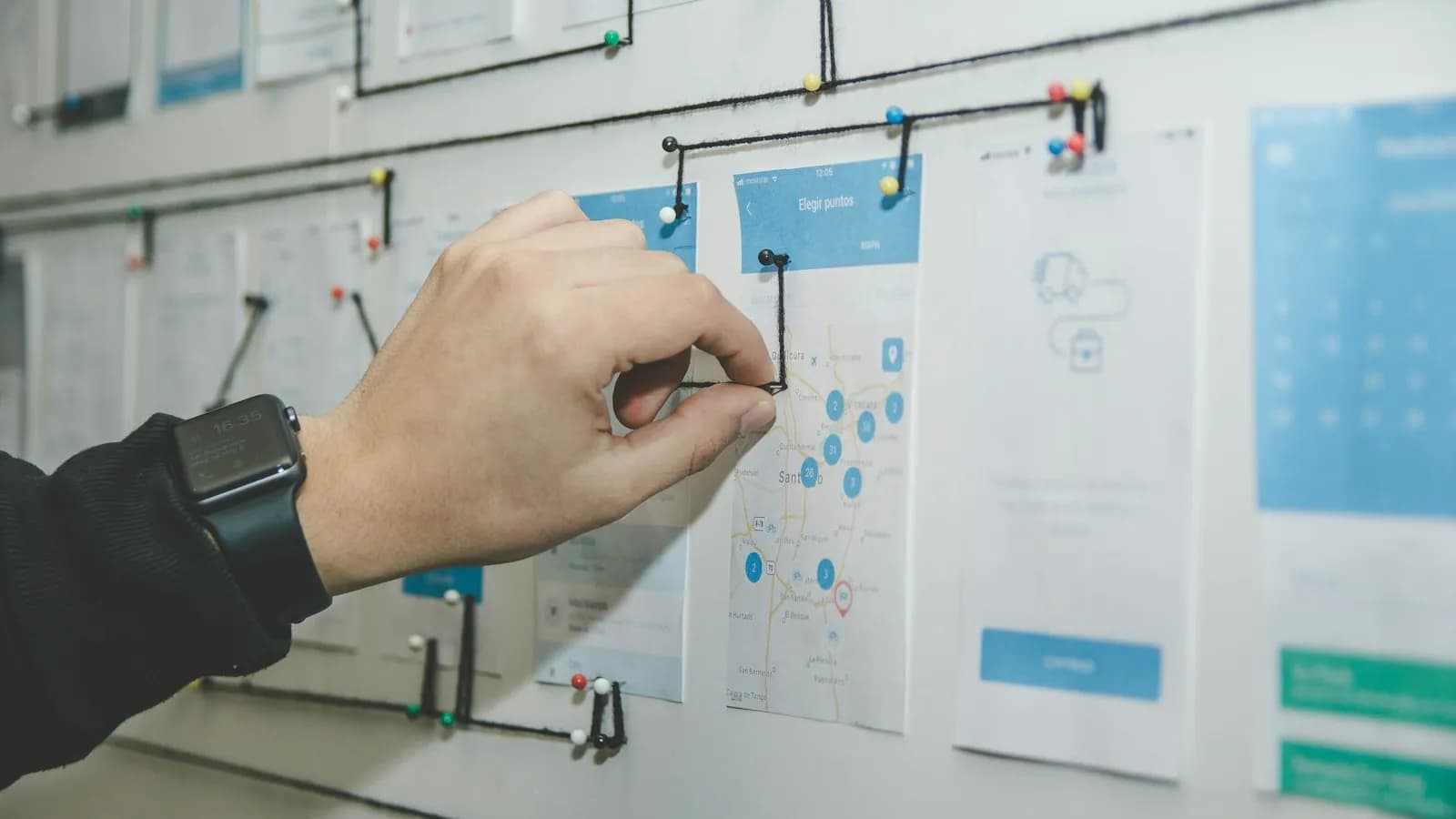 A hand pinning paper screen designs to a wall during planning