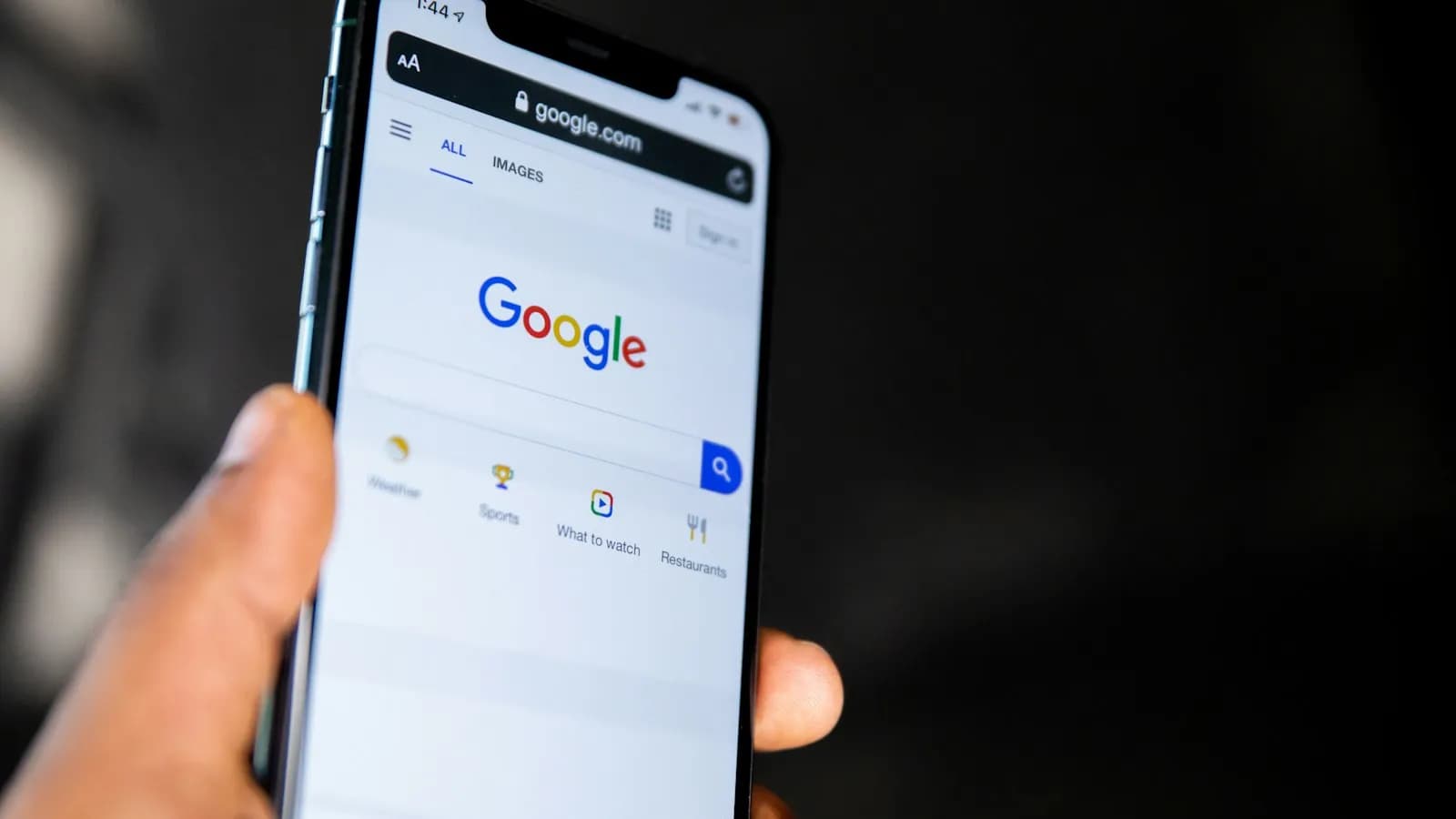 A hand holding a smartphone showing the Google search home page