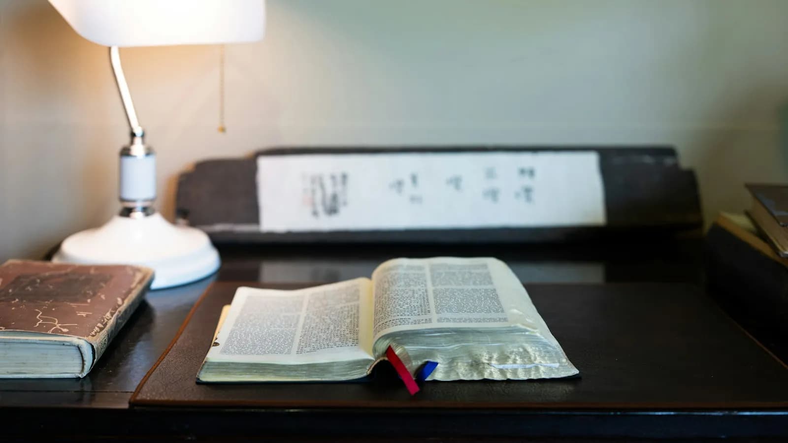 An open book on a wooden desk under a reading lamp