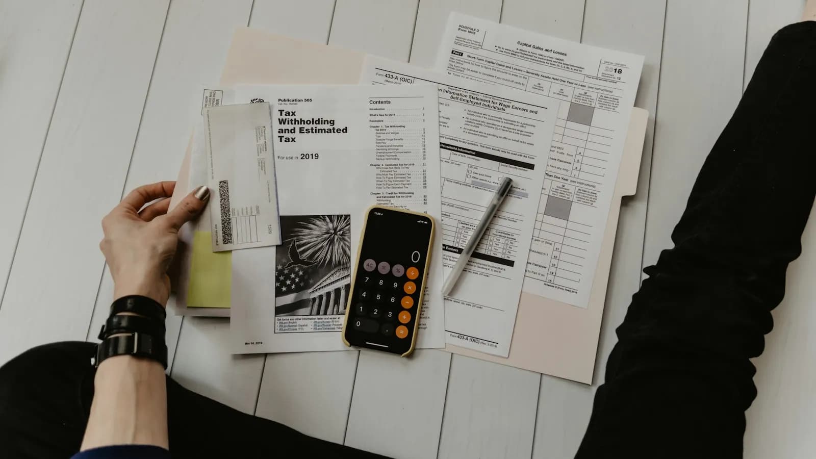 A person working with a calculator, pen and printed tax forms on a desk