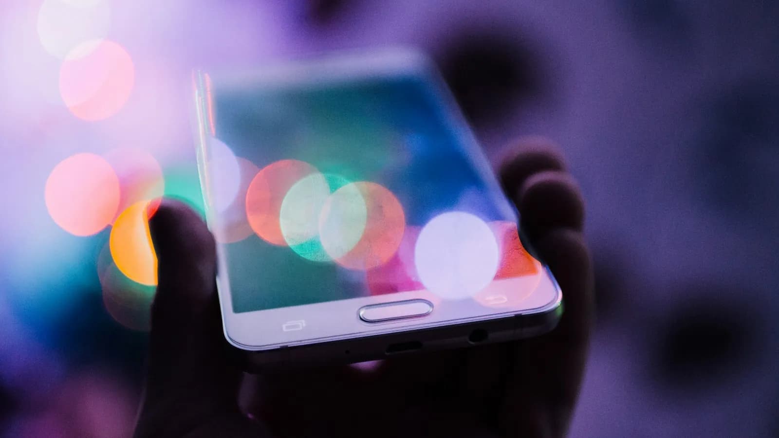A hand holding a smartphone against a background of colourful lights