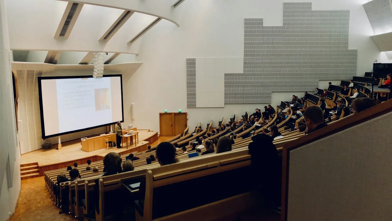 A large lecture hall with rows of students facing a projection screen