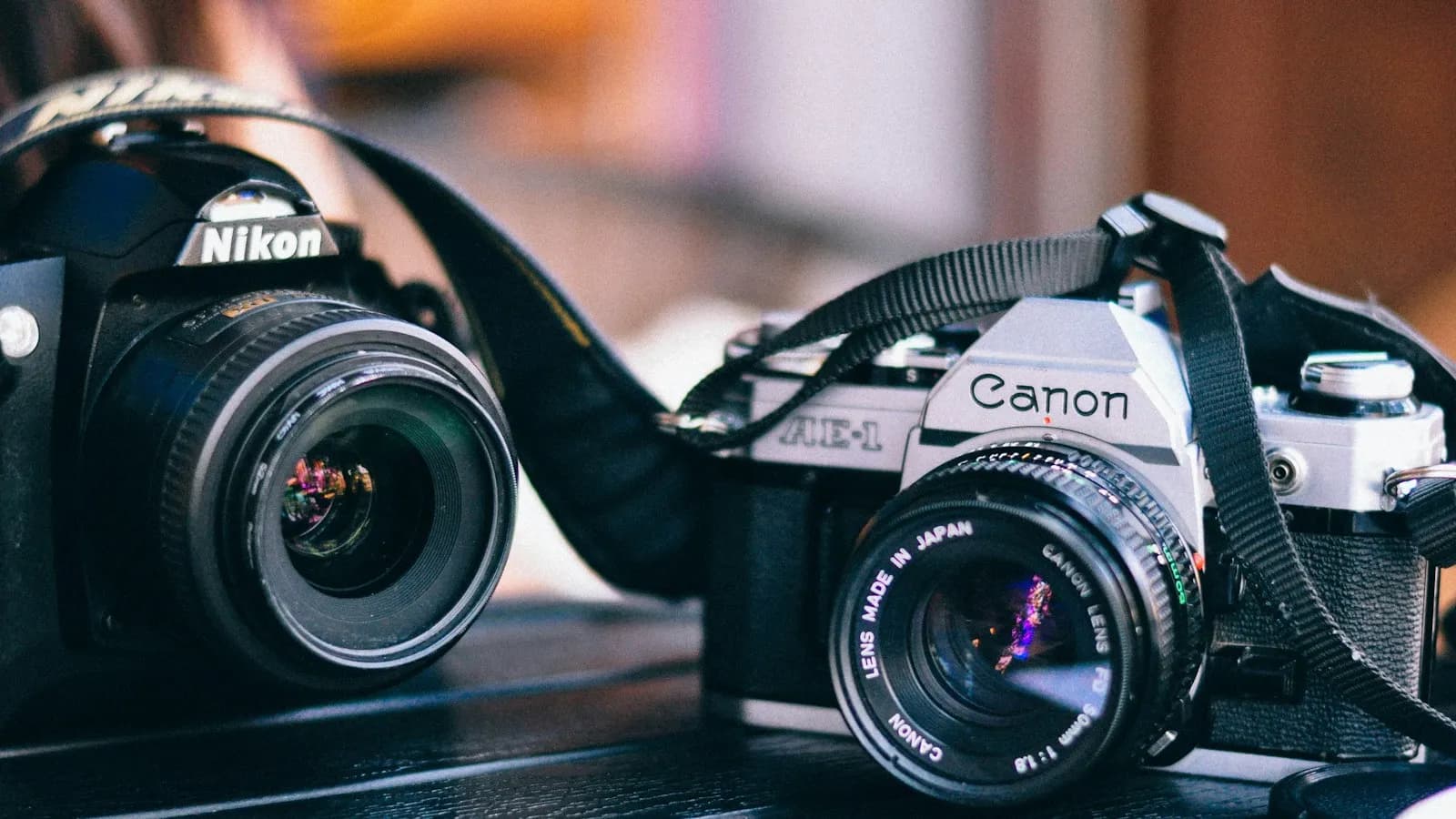 A Nikon and a Canon film camera side by side on a dark table