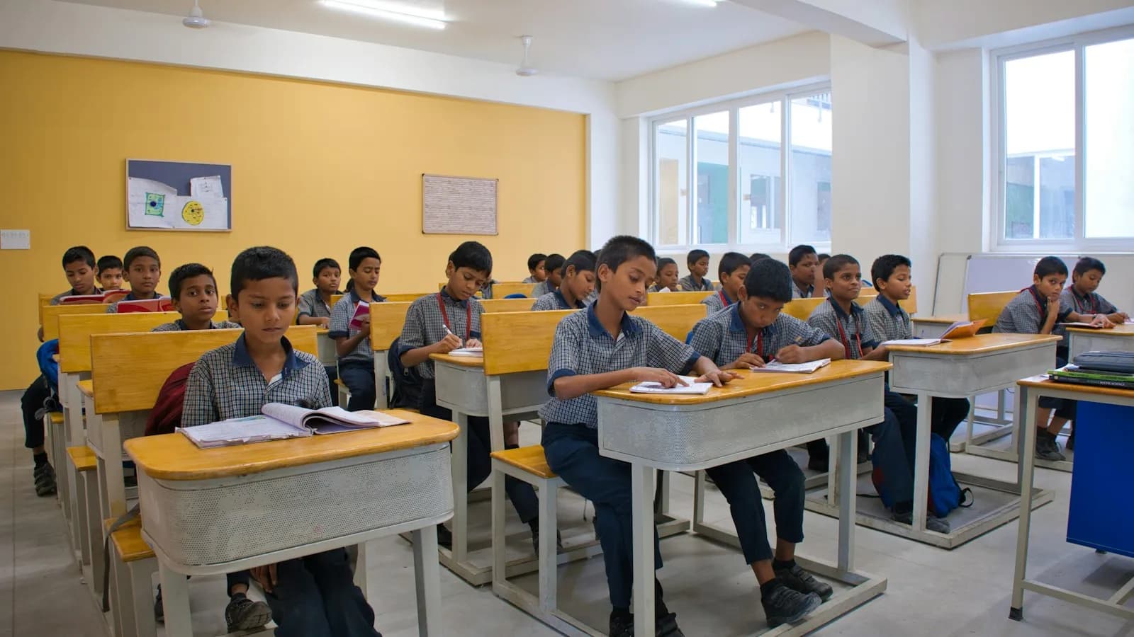 Students in uniform sitting at desks in a bright classroom with yellow walls