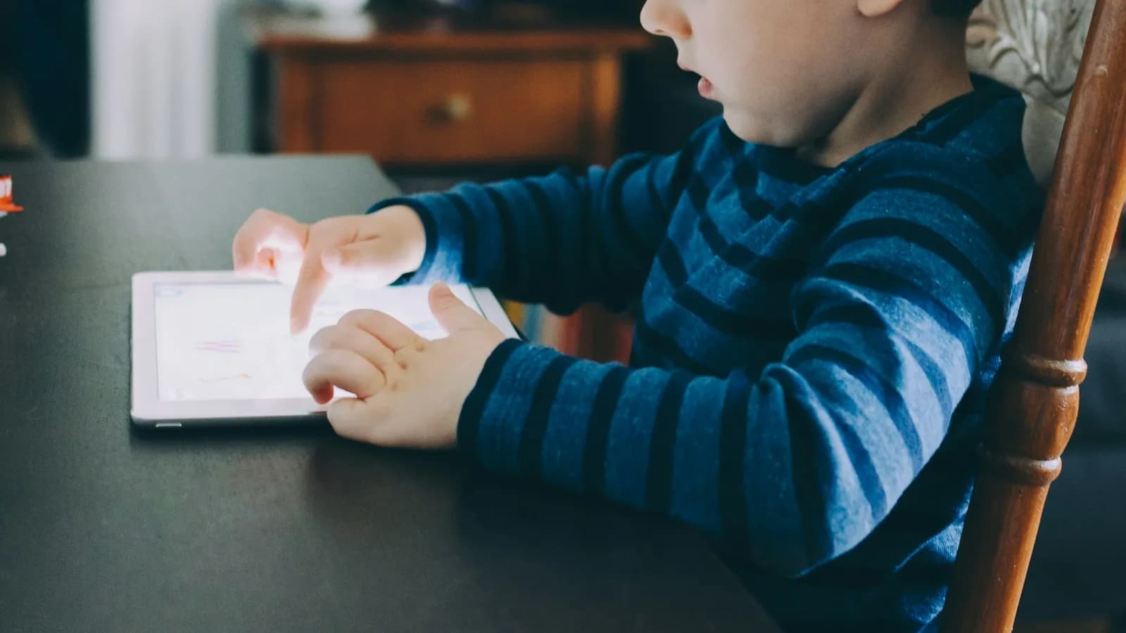 A young boy in a striped sweater using a tablet at a table