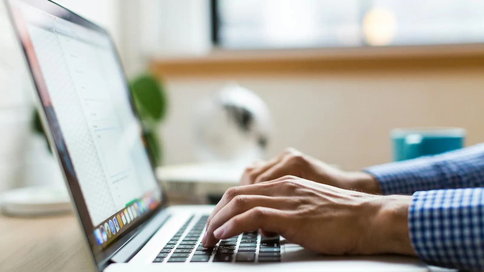 Hands typing on a silver laptop keyboard at a desk