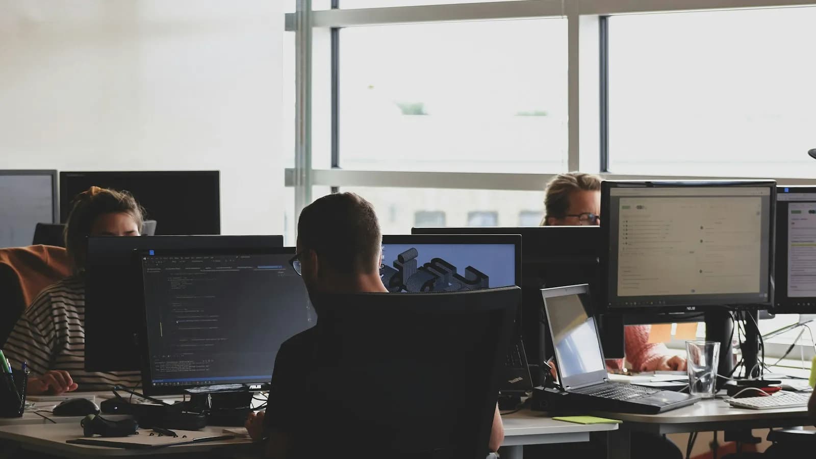 Staff working at computers with several monitors in a bright open-plan office