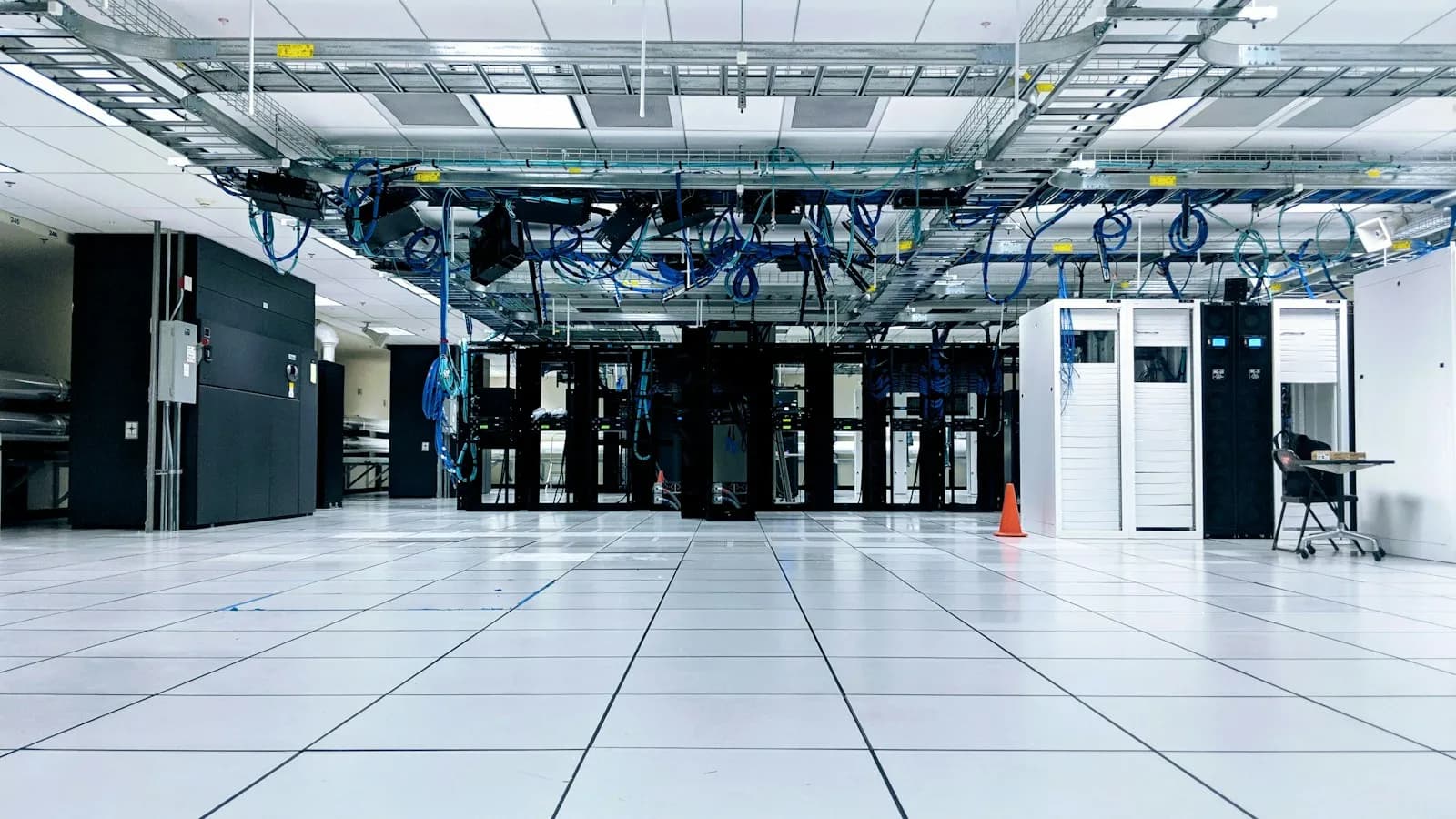 A bright server room with rows of black and white cabinets under blue cables