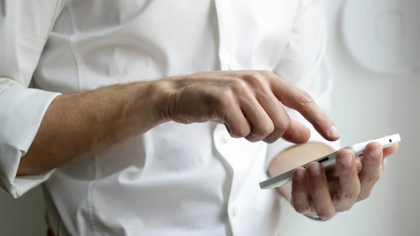 Close-up of a person in a white shirt holding a white smartphone and tapping the screen