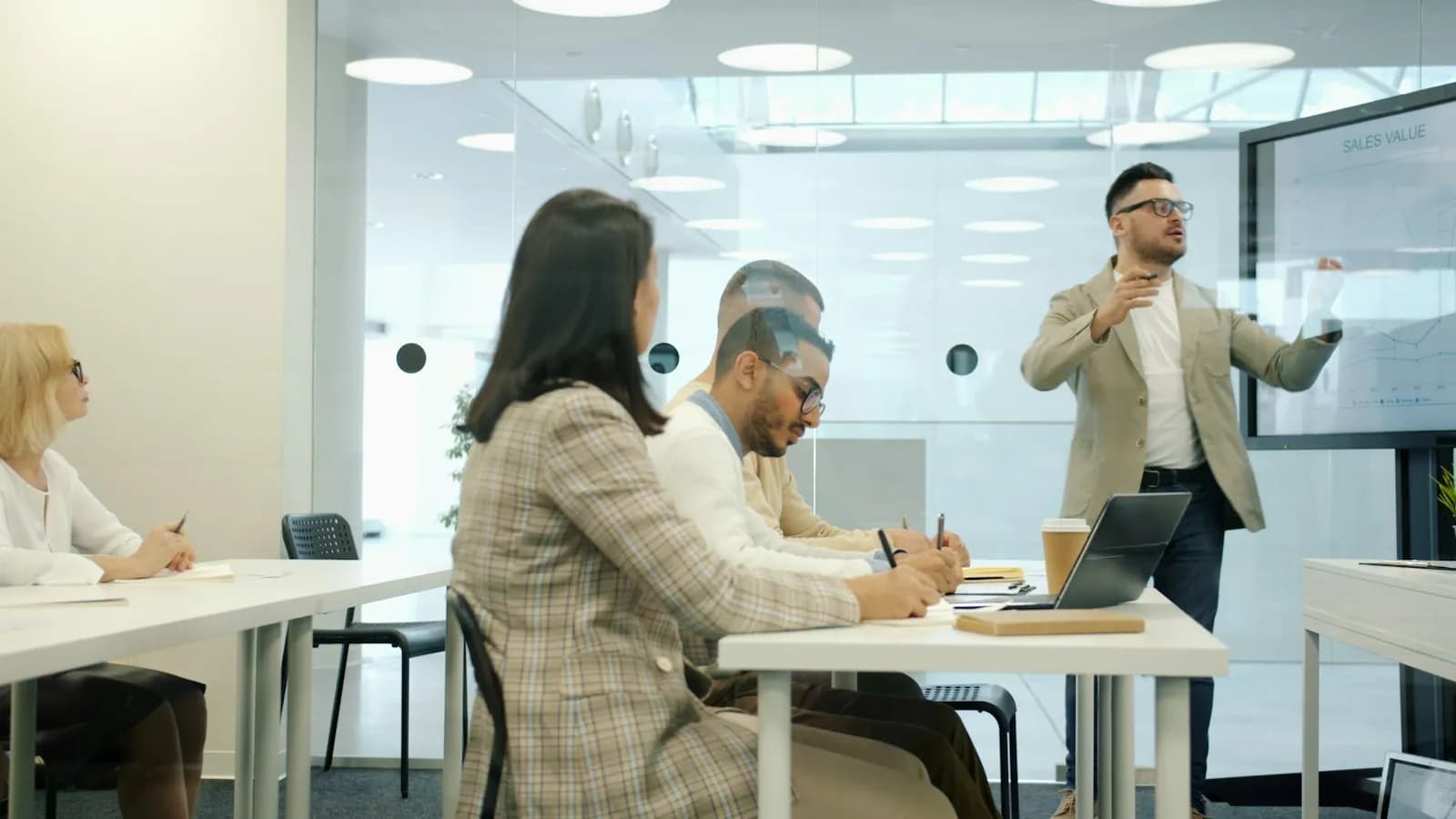 A man presenting to colleagues seated around a table in a modern glass-walled meeting room